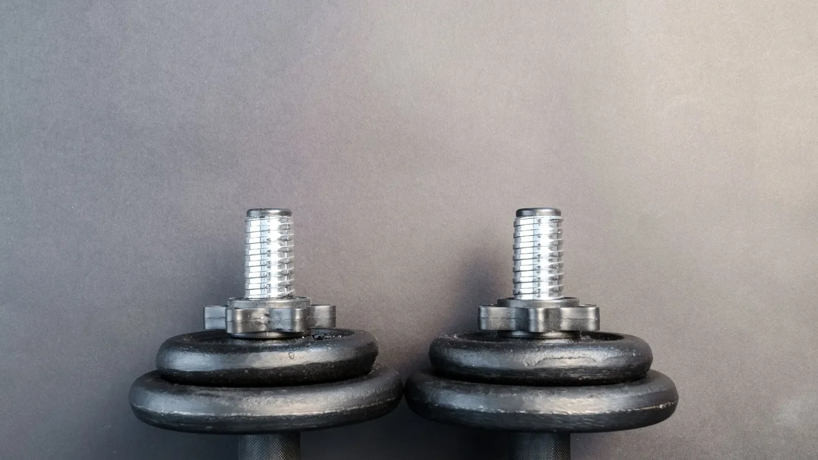 Adjustable dumbbell set beside fixed hex dumbbells on a rubber gym floor, showing the size difference
