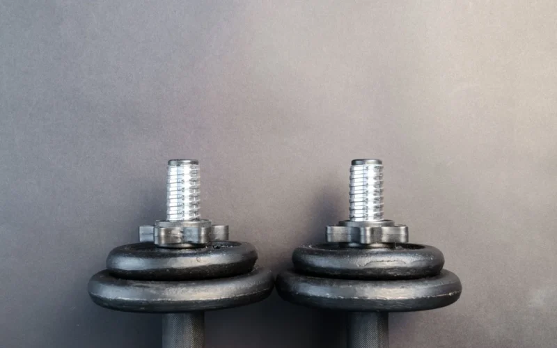 Adjustable dumbbell set beside fixed hex dumbbells on a rubber gym floor, showing the size difference