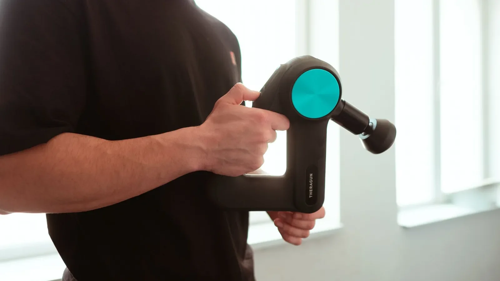 Theragun Mini massage gun placed next to a standard water bottle to show its compact travel size