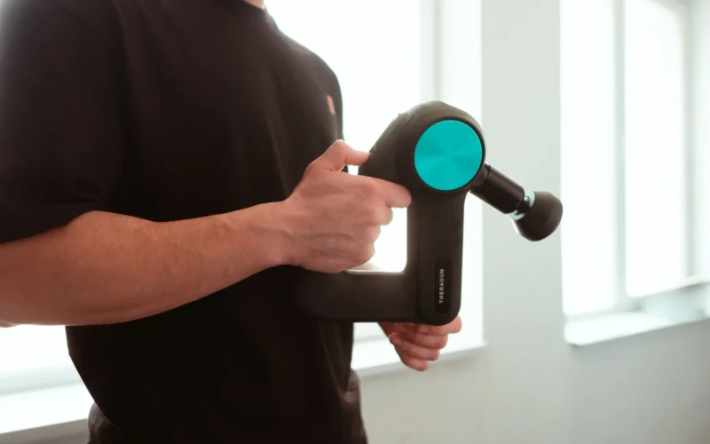 Theragun Mini massage gun placed next to a standard water bottle to show its compact travel size