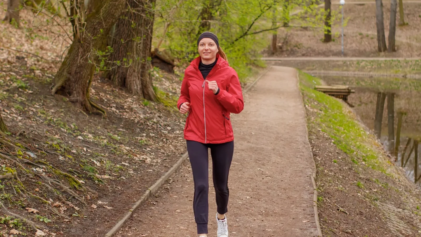 Runner in athletic wear jogging on a park path during daytime with trees in background