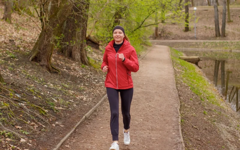 Runner in athletic wear jogging on a park path during daytime with trees in background
