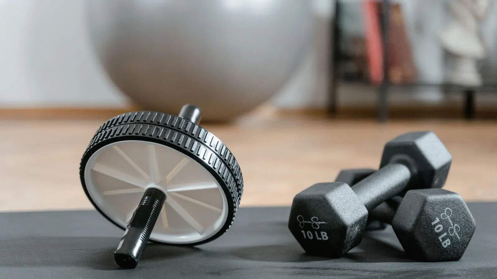 Adjustable dumbbells, resistance loop bands, and doorway pull-up bar arranged on a foam mat in a home gym corner