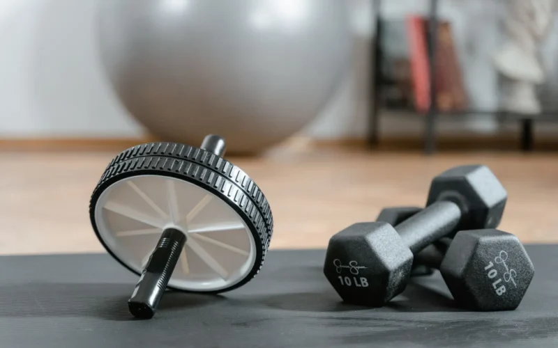 Adjustable dumbbells, resistance loop bands, and doorway pull-up bar arranged on a foam mat in a home gym corner