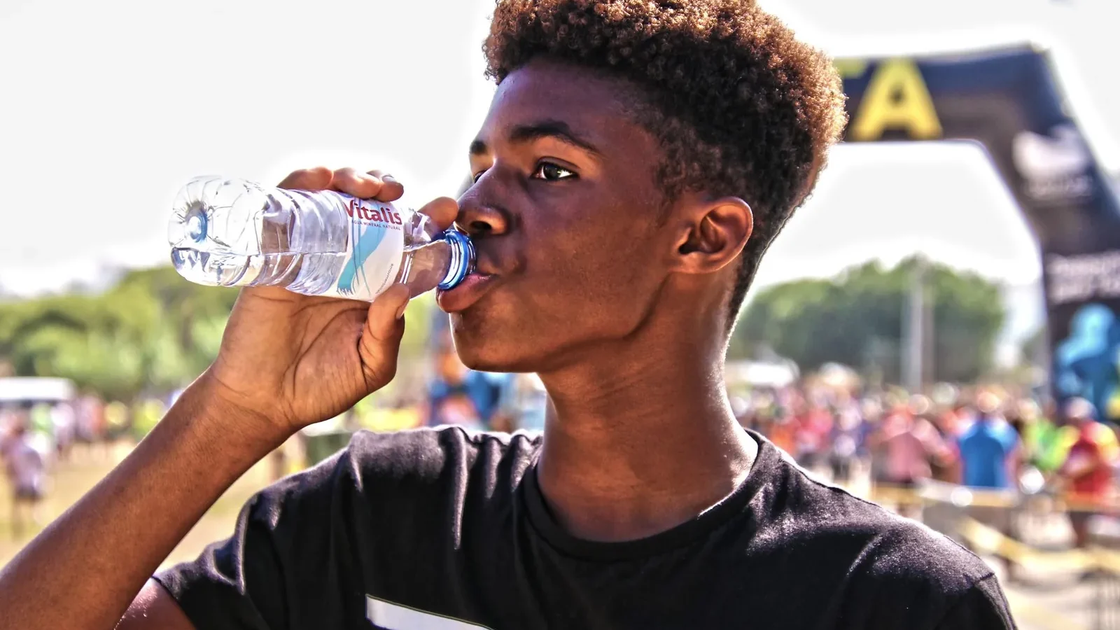 Athlete drinking from a handheld bottle mid-stride on a sun-exposed trail run