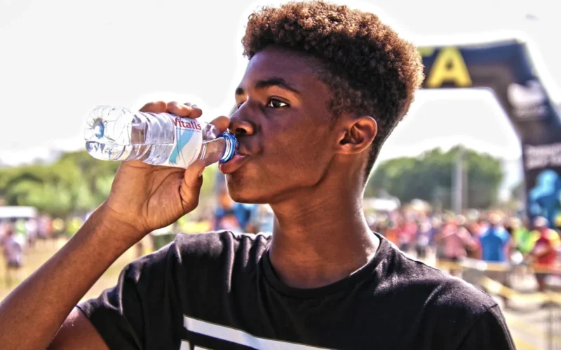Athlete drinking from a handheld bottle mid-stride on a sun-exposed trail run