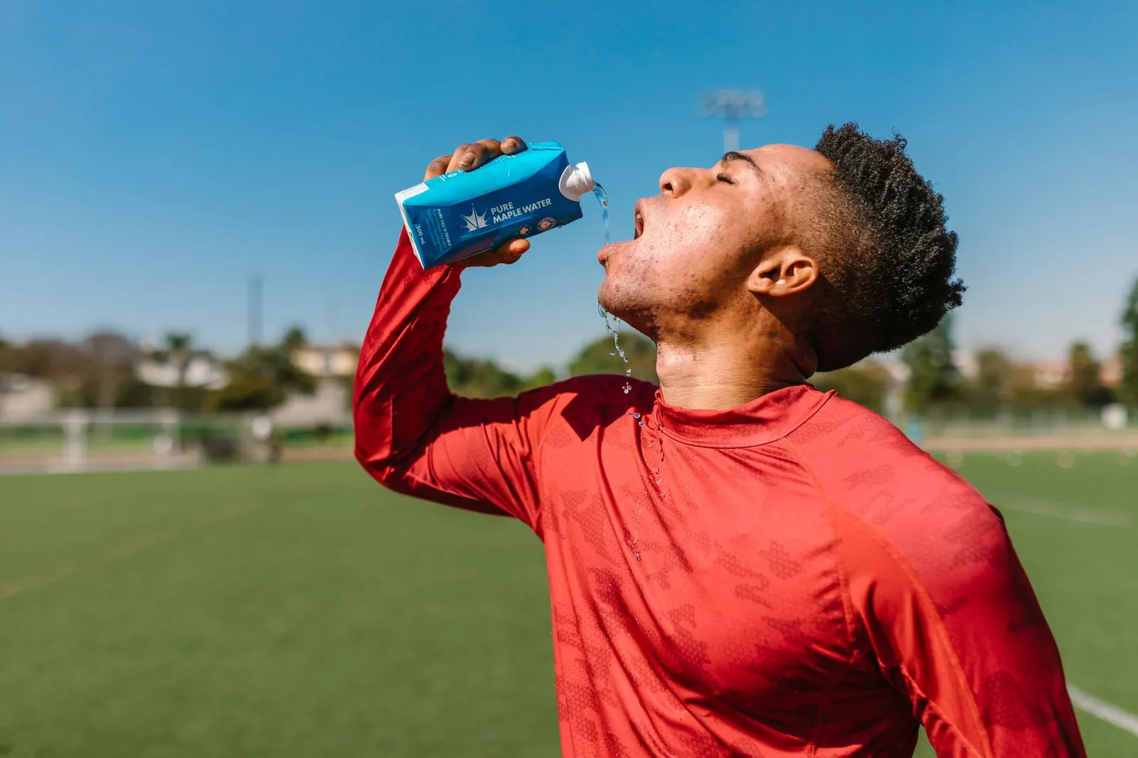 Athlete drinking from a handheld bottle mid-stride on a sun-exposed trail run