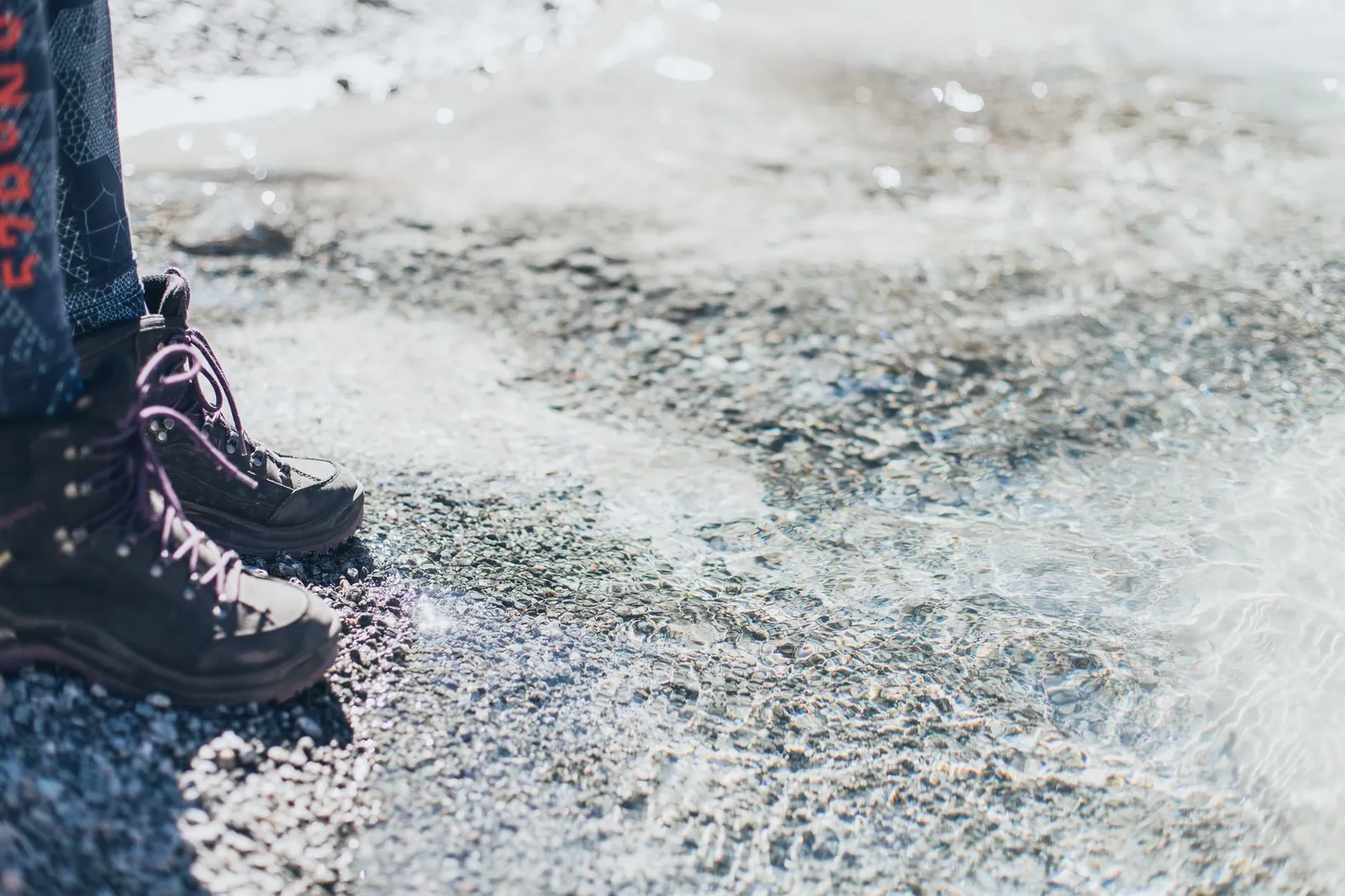 Hiker descending a loose-rock slope wearing sturdy hiking boots with reinforced ankle collar and aggressive lug sole